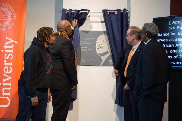 Chancellor Syverud, Barry Wells, and others, stand next to curtain as they unveil the Dr. King plaque at Shaffer Hall