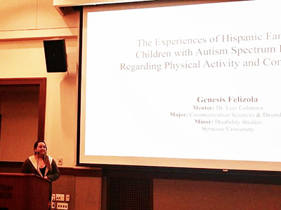 Genesis Felizola stands in front of a screen showing her research