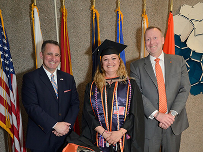 female graduate in cap and gown, flanked by two male adults