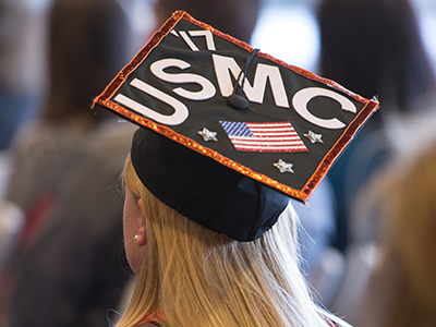 female veteran from the back with USMC and US flag on her graduation cap
