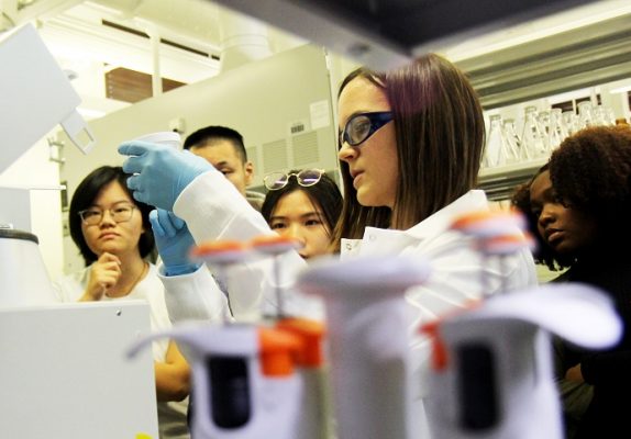 woman working in lab surrounded by a few people