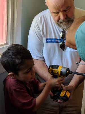 man helping boy using power tool to build bed