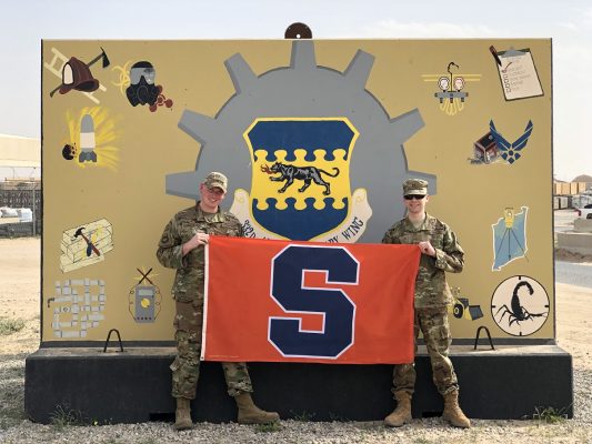 two men in uniforms holding flag with S