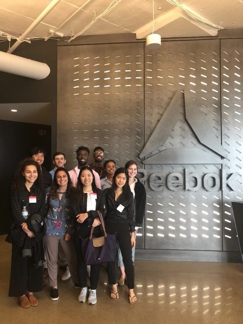 Students in business clothes standing in front of Reebok logo