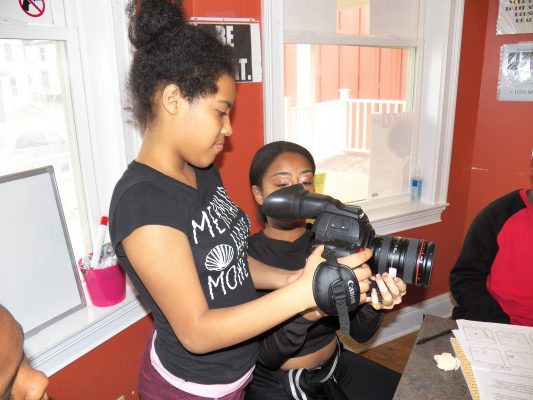 Students holds camera while Simone instructs her.