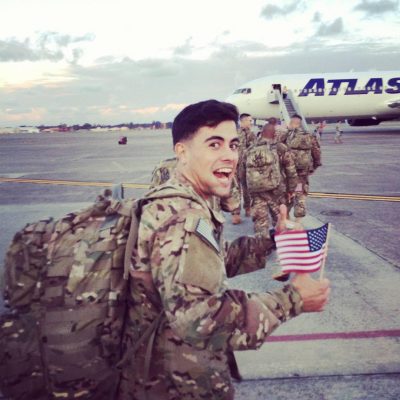 man in military uniform waving American flag in front of airplane