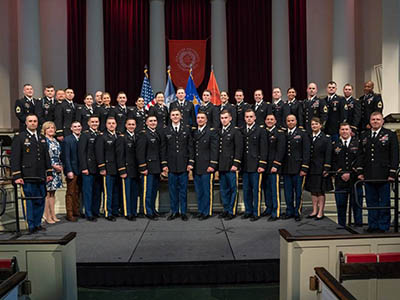 Cadets and other military personnel in uniform lined in two rows on the chapel stage.