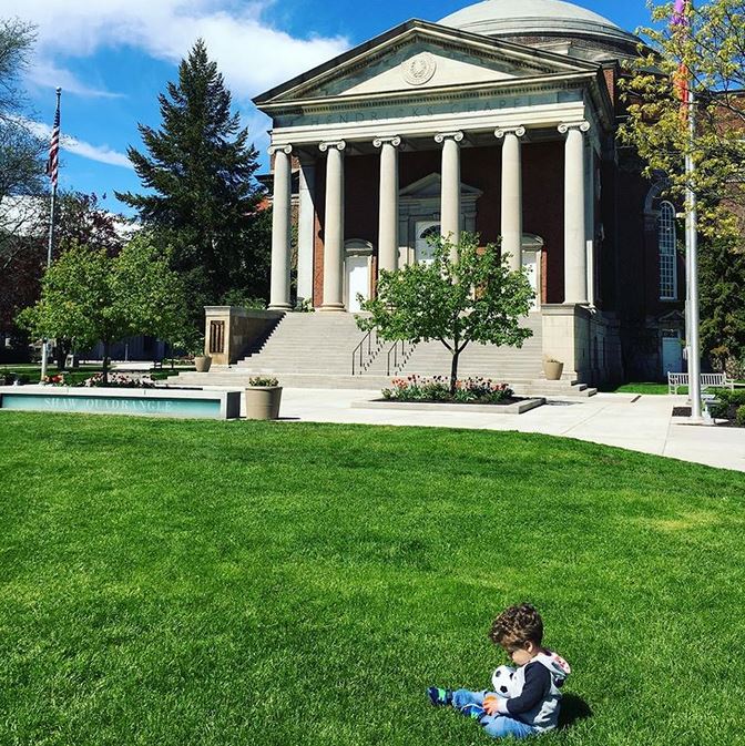 small child sitting on lawn in front of Hendricks Chapel