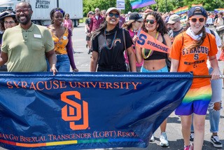 Folks marching in Pride Parade holding Syracuse University LGBT Resource Center banner, wearing Syracuse University apparel and holding Syracuse University flag