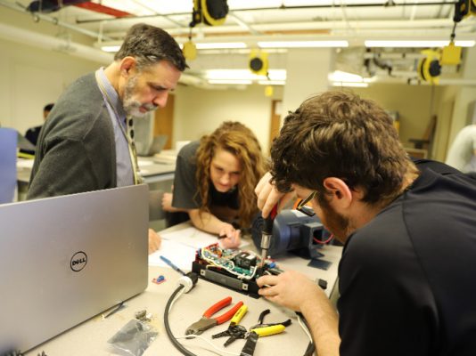 three people working with tools on electrical component