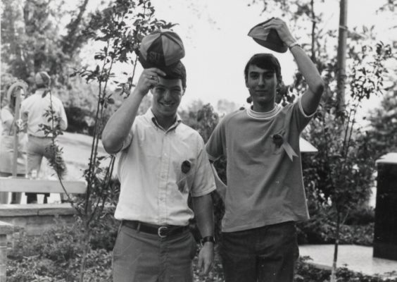 Two students holding hats over their heads.