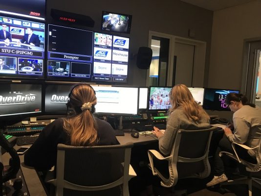 three people sitting in front of computer and television screens