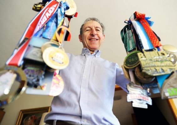man holds up a plethora of athletic medals