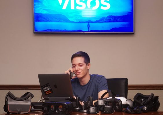 Young man sitting at computer with VISOS sign above him.