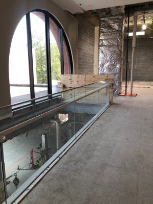 The interior of Schine Student Center, currently under construction. Duct work is in the background and a large window looks out to some trees. Construction equipment and piping is on the floor below.