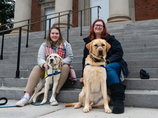 two women sitting with two dogs on steps of Hendricks Chapel