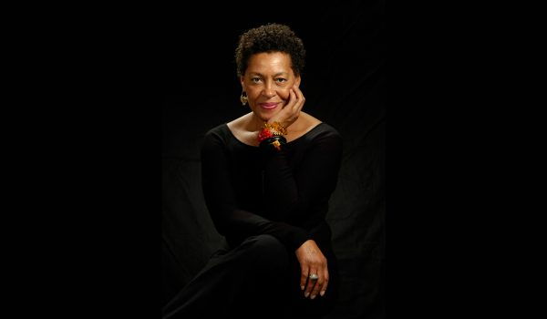 African American woman in black dress posing in front of a black background