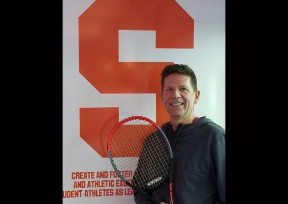 man posing with tennis racquet in front of Syracuse emblem
