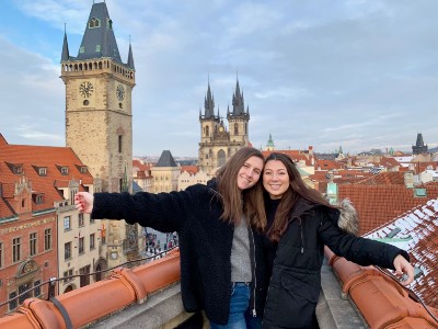 two female students on a rooftop with gothic buildings behind them