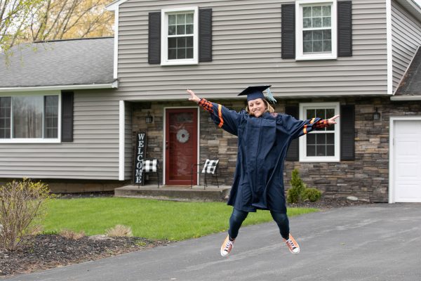 person in graduation gown jumping in driveway