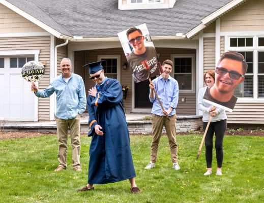 graduate standing in front yard with family members