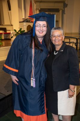 two people standing together, one in graduation gown