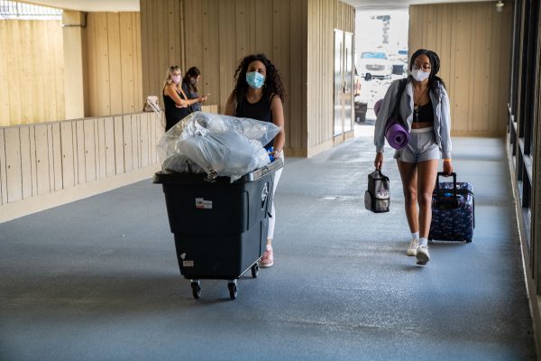 two people with masks pushing bin and carrying belongings into residence hall