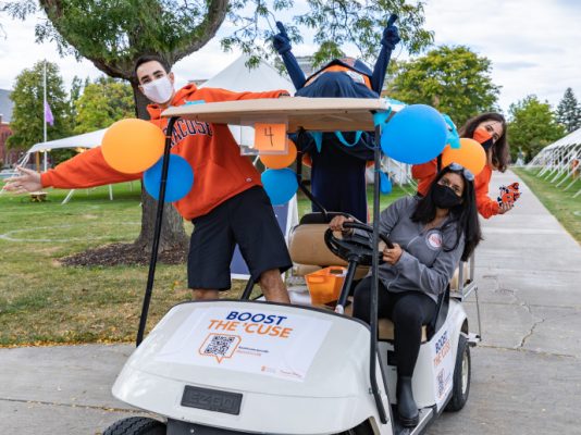 three people and Otto riding around in golf cart on the Quad on Syracuse University campus