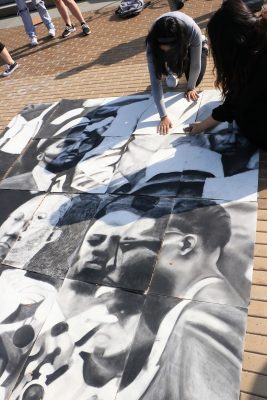 students place drawings in a collection of drawings as part of a mosaic on the Einhorn Family Walk