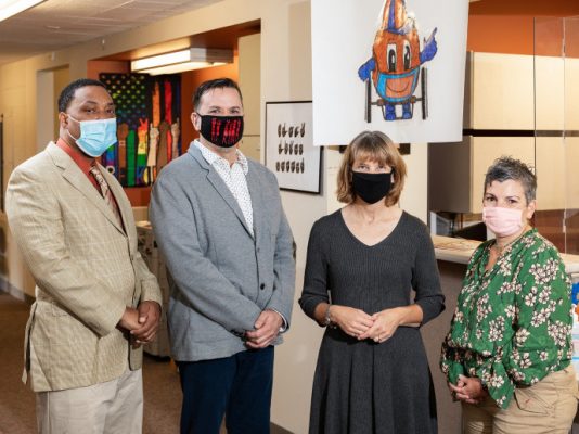 four people standing in corridor wearing masks