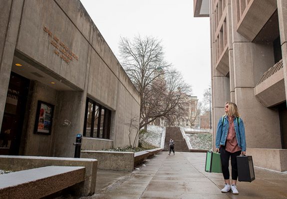 student with luggage looking at campus building