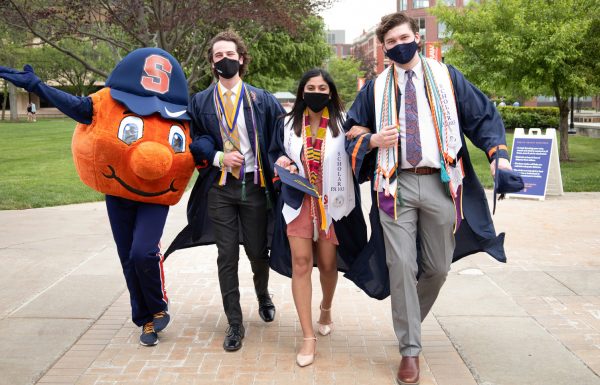 three students walking outside with Otto during Commencement