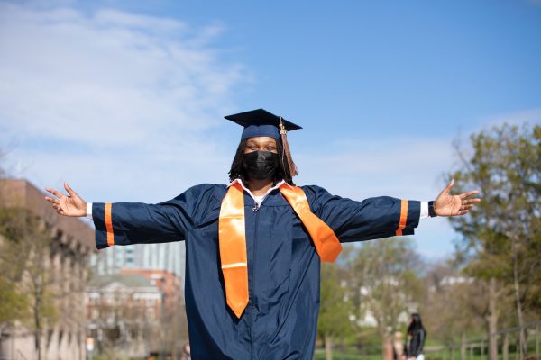 student in cap and gown stands with arms outstretched outside during Commencement 2021