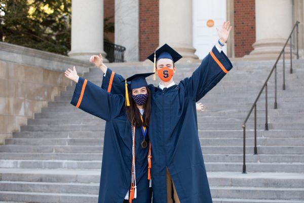 two students in caps and gowns with their arms in the air during Commencement 2021