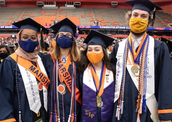 four people in caps, gowns and assorted regalia pose during Commencement 2020, held Sept. 19, 2021, in the stadium