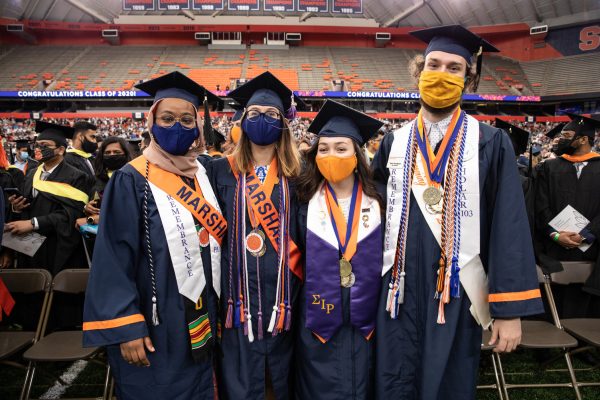four people pose in caps, gowns and an assortment of regalia at Commencement 2020, held Sept. 19, 2021 in the stadium