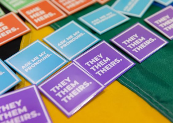 Pins displaying various pronouns on a table