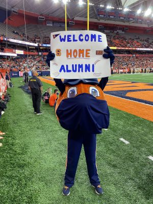 Otto holds a sign in the stadium that says "Welcome Home Alumni" during football game, Orange Central 2021