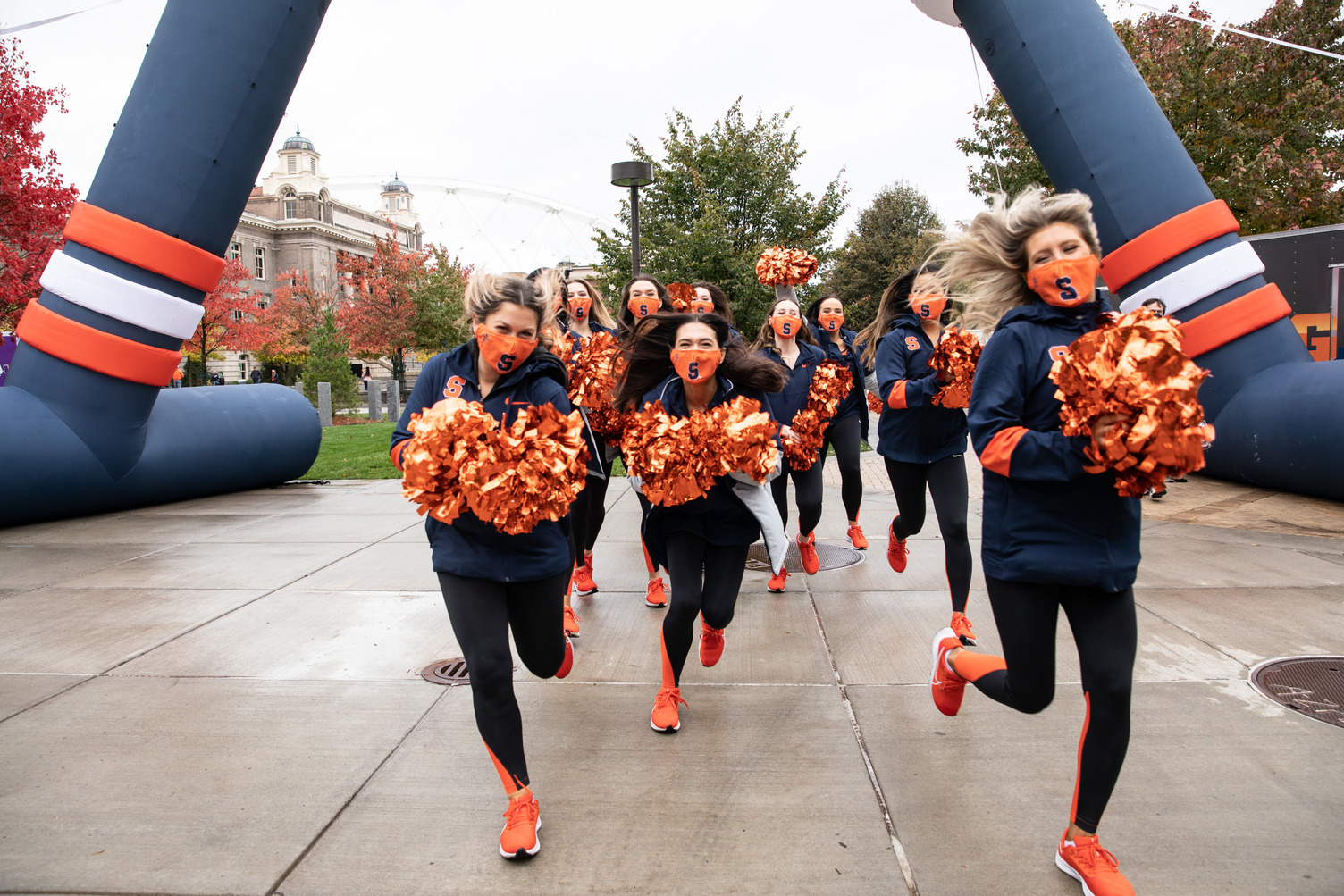 cheerleaders run through an inflatable arch at Orange Central tailgate celebration