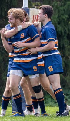 three rugby players hugging on field