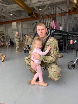 person in uniform hugging child in hangar
