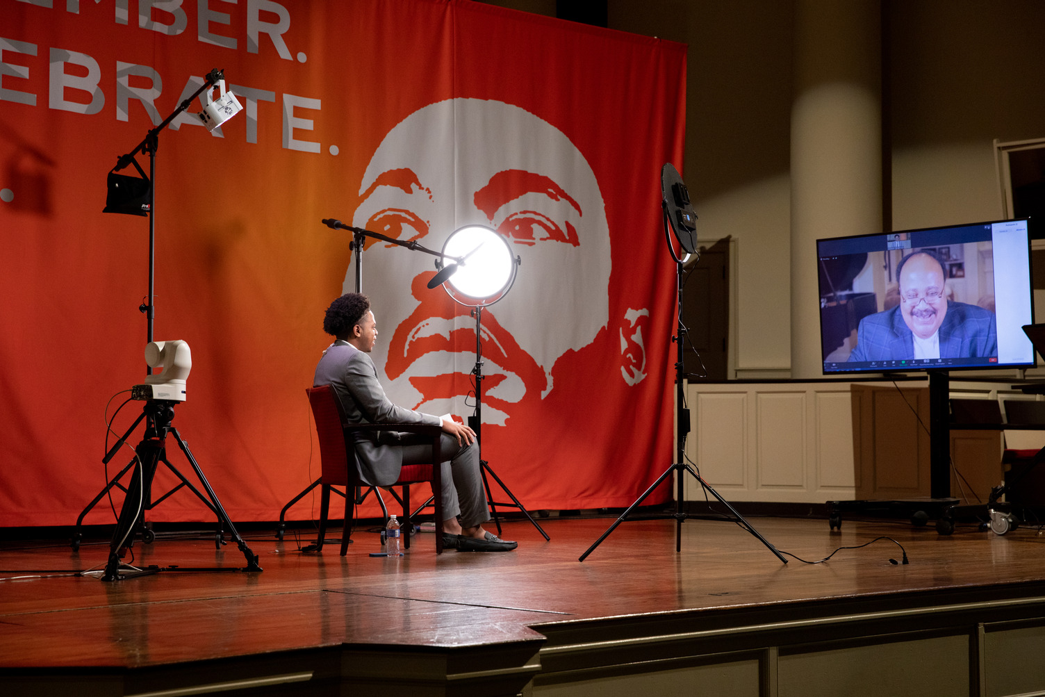 person sitting on stage talking to another person in video conference