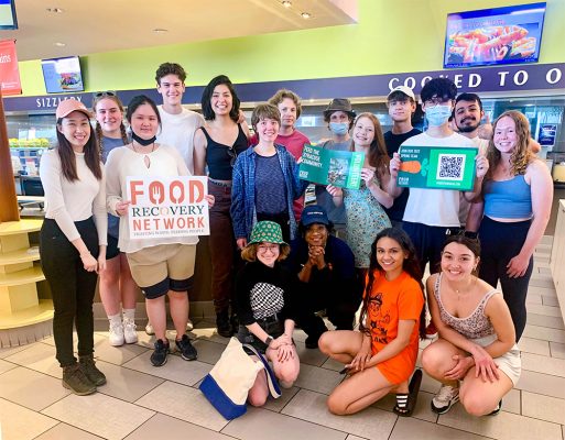 student volunteers with the Food Recovery network pose and hold up signs in Graham Dining Center