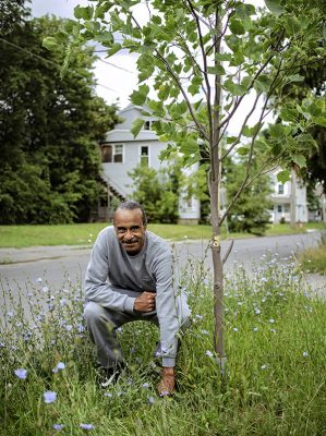 photo taken of Clifford Ryan posing by a tree planted in memory of his son on Syracuse's South Side during the 2021 Photo Walk