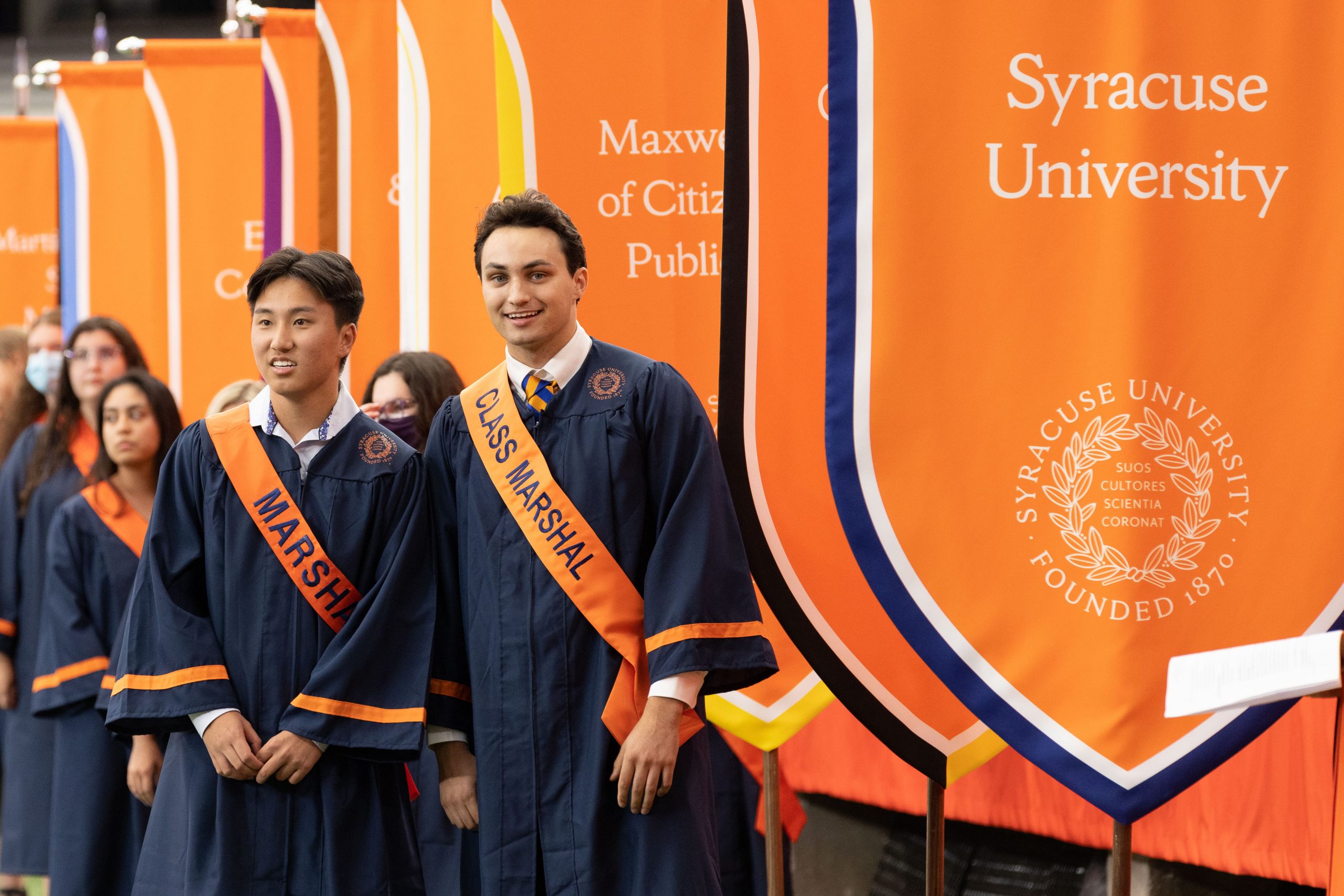 group of students, led by two class marshals, amidst a row of Syracuse University flags at 2022 New Student Convocation