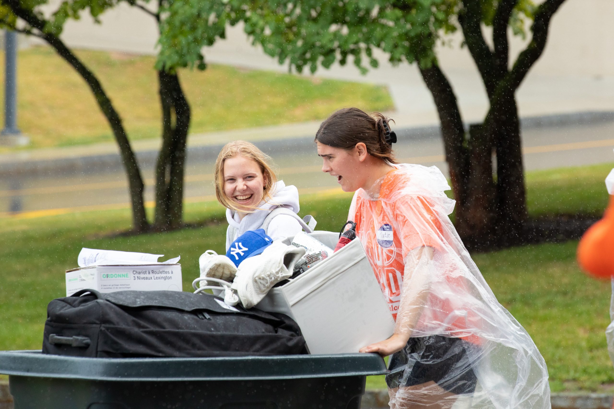 a member of the Goon Squad pushes a rolling bin alongside a new student during move-in