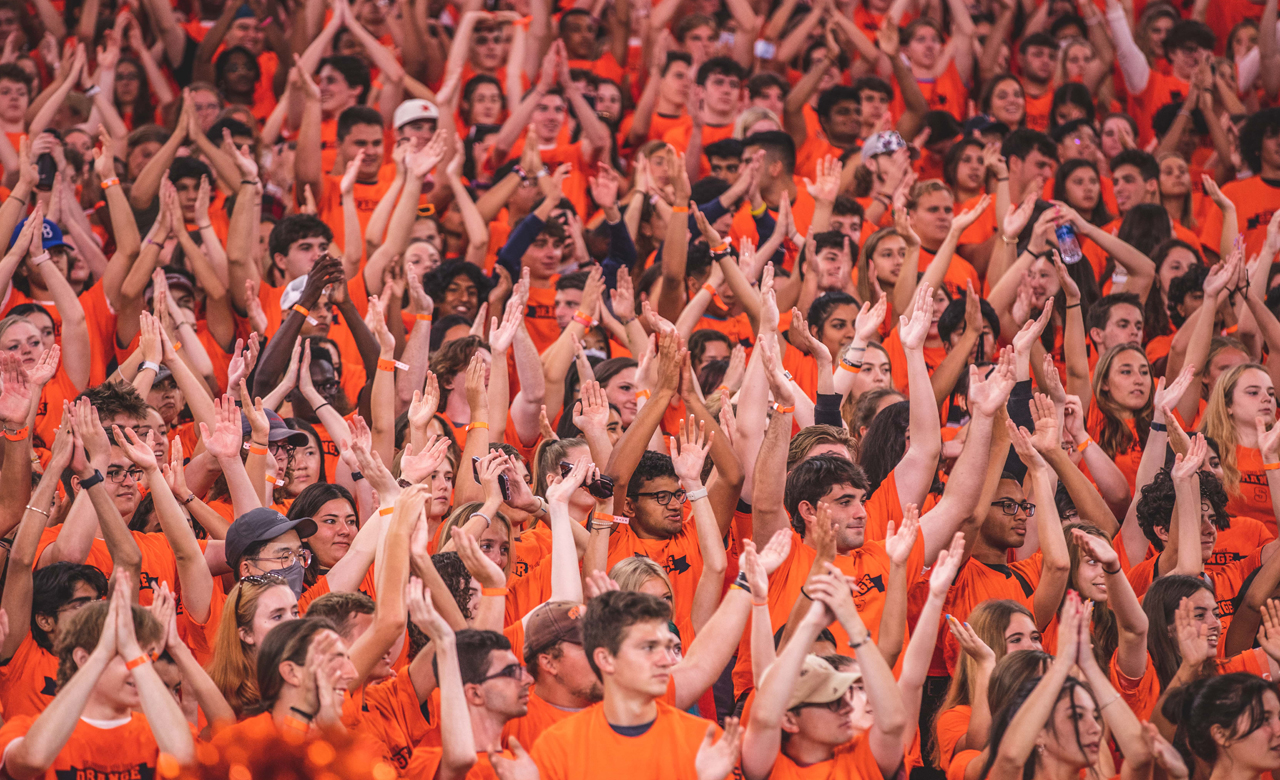 dozens of students in orange t-shirts with their hands in the air during Syracuse Welcome