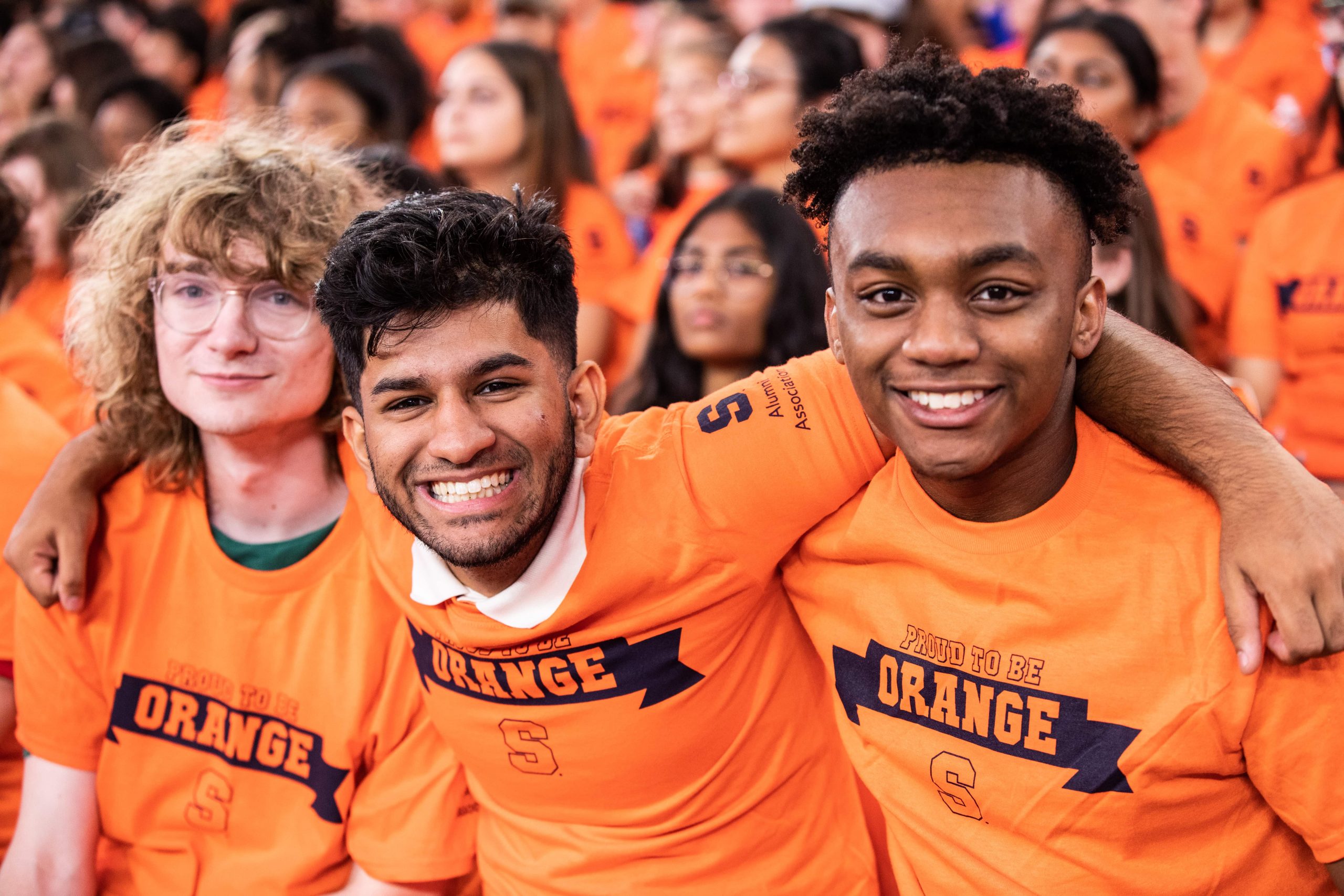 three students wearing Orange t-shirts wrap their arms around each other and smile for a photo during "Dome Sweet Dome"