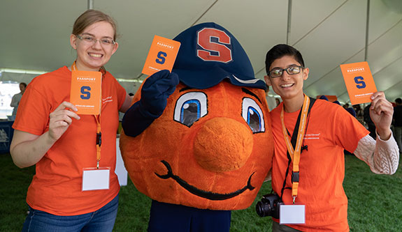Mascot Otto with two students who are holding "passports"