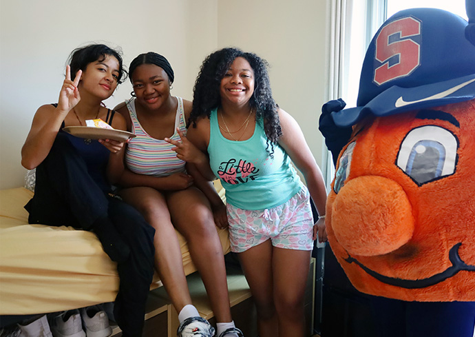three students pose with Otto in a residence hall during Summer College at Syracuse University